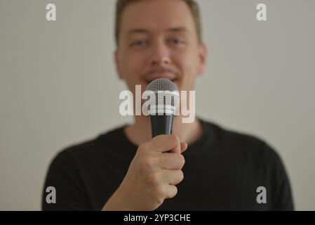 A man speaker smiling with microphone. Blurred image with focus on a hand foreground. Stock Photo