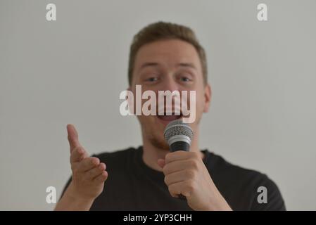A man emotionally singing song in microphone and smiling. Blurred image with focus on a hand foreground. Stock Photo