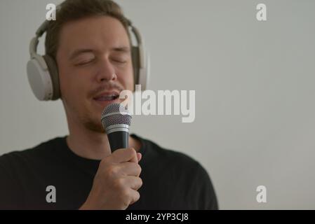 A man wearing headphones emotionally singing in microphone with eyes closed. Blurred image with focus on a hand foreground. Stock Photo