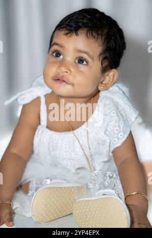 A child in a stylish white outfit, complete with a matching headband and floral dress, radiating elegance and charm. Stock Photo