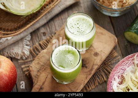 Two shot glasses of green cabbage juice with cucumber and apples on a table Stock Photo