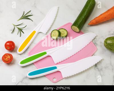 Various plastic knifes for children and chopped vegetables on the table Stock Photo