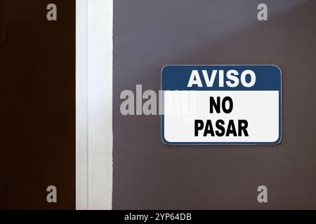 Blue and white notice sign on the side of an open door stating in Spanish 'Aviso, No pasar', meaning 'Notice, No passing'. Stock Photo