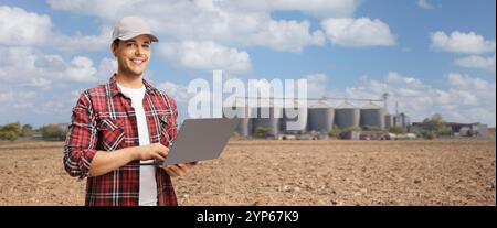 Farmer holding a laptop computer on a field with agricultural silos towers Stock Photo