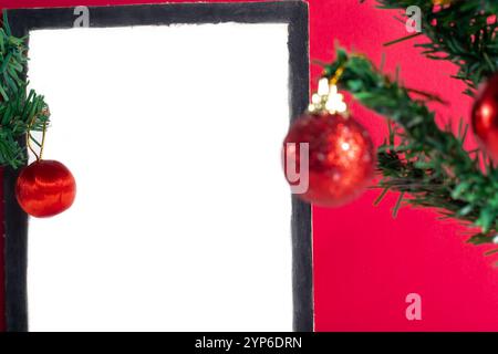 A minimalist white empty frame surrounded by festive Christmas ornaments and decorations on a vibrant red background Stock Photo