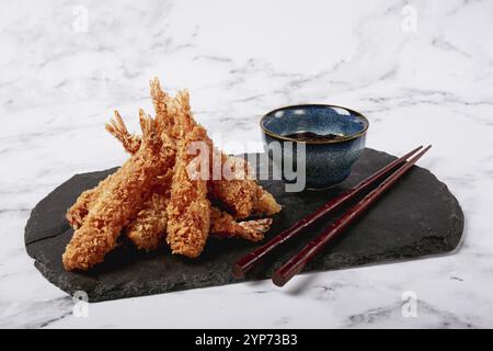Shrimp in tempura, deep fried, on black slate, with sauce, light marble table, no people Stock Photo