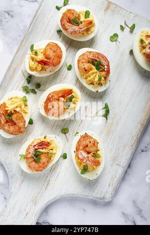 Boiled eggs stuffed with yolk and seasoned with mayonnaise, stuffed eggs with shrimp, on a white wooden chopping board, selective focus, close-up, wit Stock Photo