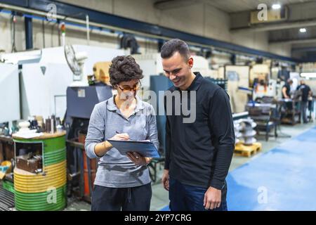 Businesswoman with male caucasian worker talking and inspecting a cnc factory writing notes on clipboard Stock Photo