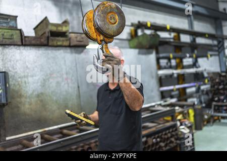 Mature caucasian man holding the hook of an industrial crane while operating in a factory Stock Photo