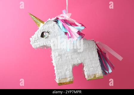 Bright pinata in shape of unicorn hanging on pink background Stock Photo