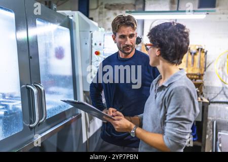 Female manager writing notes in a clipboard and manual worker talking in a factory Stock Photo