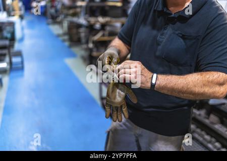 Cropped photo of an unrecognizable mature male caucasian worker putting on protective gloves in a factory Stock Photo