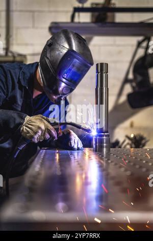 Vertical photo of a concentrated male caucasian welder with protective gear working in a factory Stock Photo