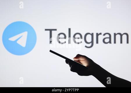 In this photo illustration, the Telegram logo seen in the background with a silhouette hand holding a smartphone Stock Photo