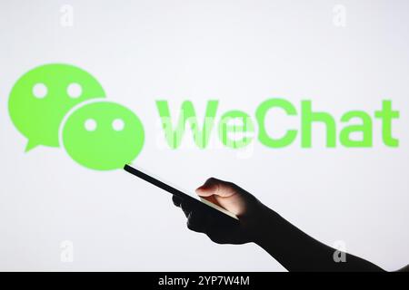 In this photo illustration, the WeChat logo seen in the background with a silhouette hand holding a smartphone Stock Photo