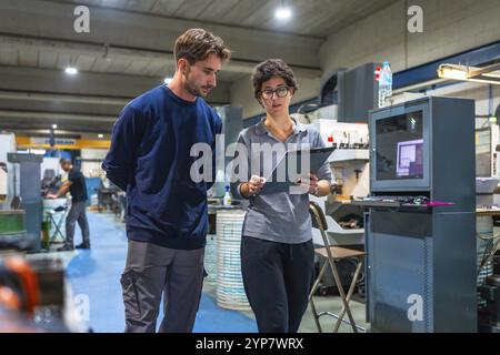 Female manager and male young engineer doing paperwork standing and talking at factory Stock Photo