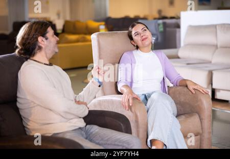 Guy and girl sitting in armchairs and deciding on buying in furniture section Stock Photo