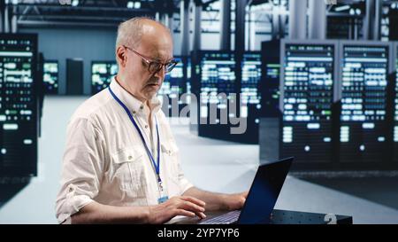 Competent inspector expertly managing data while navigating in industrial server room. Experienced system administrator ensuring optimal cybersecurity protection, optimizing systems Stock Photo