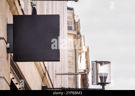 A blank black rectangular shop sign mounted on a building, ideal for branding or store identification in a commercial district. Stock Photo