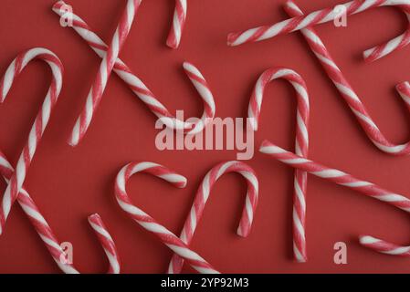 Top view image capturing multiple red and white striped candy canes arranged on a vibrant red background. Stock Photo