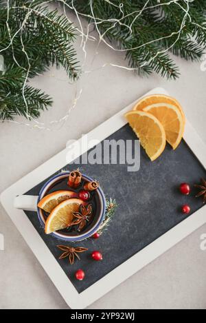 Mug with hot drink, mulled wine with orange slice, cranberry and cinnamon sticks on framed blackboard and fir tree branches on background, top view Stock Photo