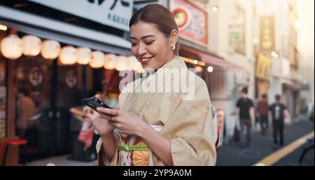 Street, travel and woman in kimono with phone, smile and online search for location on city map. Smartphone, scroll and happy Japanese girl in Stock Photo