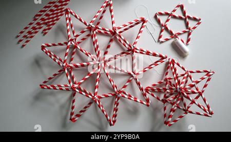 Set of handmade stars in red and white stripe. Different shape. Chaotically placed on white background. Needle, white thread, paper straws for drinks are nearby. Idea for decoration. Christmas. Photo. Stock Photo