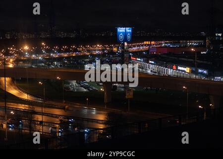 On night roads, cars drive over a bridge and a road junction. Urban cityscape Stock Photo