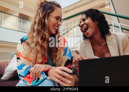 Two young colleagues share a hearty laugh while working together in a modern office environment. Their joyful expressions convey the positive and coll Stock Photo