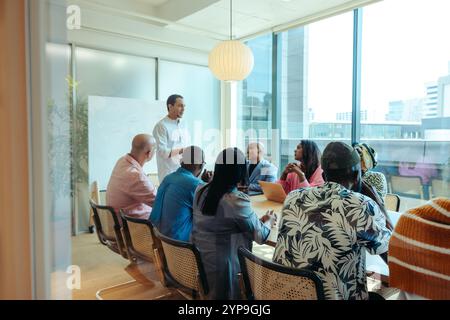 A diverse marketing team meets in a bright, modern conference room to discuss strategic planning. Professionals are seated around a table, actively en Stock Photo