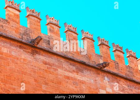 Top section of a historic stone wall with crenellations and two gargoyle sculptures protruding from the wall. Crenellations are evenly spaced and have Stock Photo
