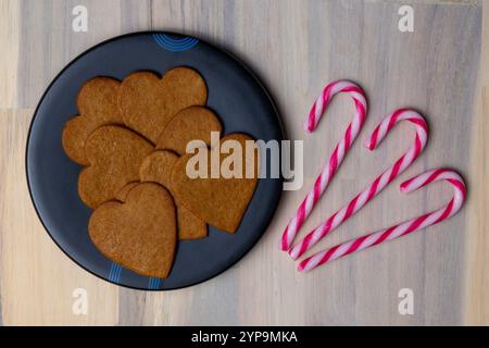 Heart-shaped cookies are neatly arranged on a dark plate next to red and white striped candy canes, perfect for holiday events. Stock Photo