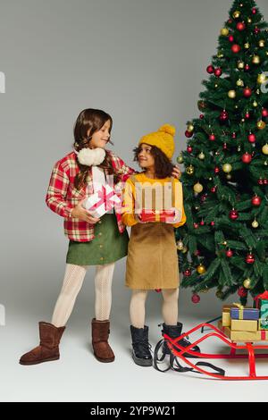 Two excited kids share the joy of Christmas while holding festive gifts by a decorated tree Stock Photo