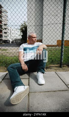 A man is sitting on the ground wearing a white shirt and blue jeans Stock Photo