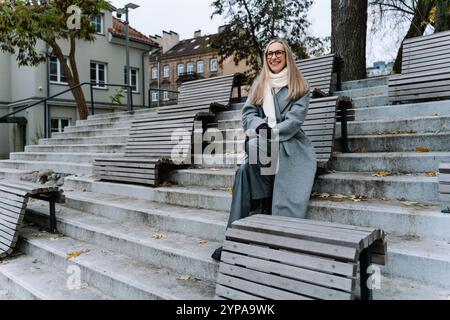 happy young woman in glasses sitting on steps in autumn Stock Photo