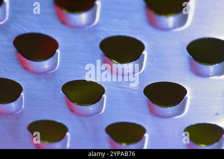Holes in a metal sheet with pink, red and blue hues Stock Photo