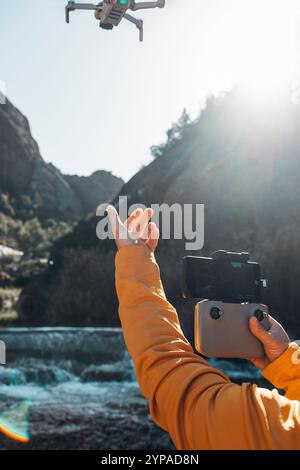 Man carefully launches drone into river in serene mountain landscape. Stock Photo