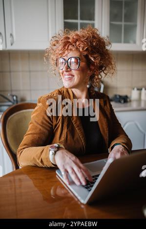Beautiful redhead middle-aged woman with curly hair working on h Stock Photo