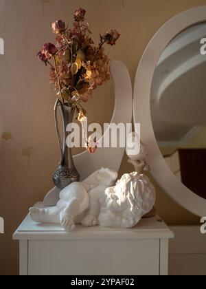 Vintage bedroom detail with dry roses, mirror and an angel statuette Stock Photo