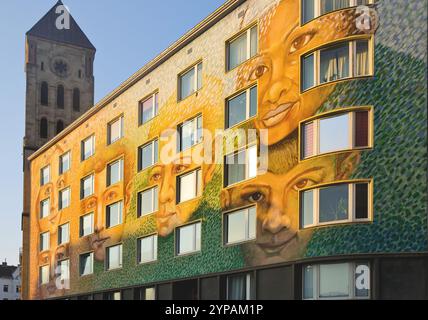 Wall of an apartment building painted with faces, street art, St. Elisabeth Church in the background, Germany, North Rhine-Westphalia, Lower Rhine, Du Stock Photo