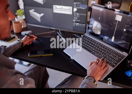 Designer is focusing on creating detailed interior models on laptop while using graphic tablet and multitasking in modern creative studio Stock Photo