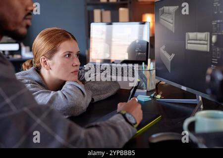 Female team member collaborating on digital design project with colleague while both focused on computer screen in modern office setting Stock Photo