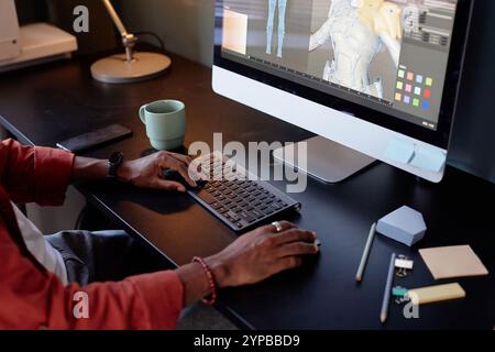 Designer working on intricate 3D models displayed on computer screen in modern office space. Various tools and gadgets are scattered on desk, hinting Stock Photo