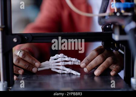 Close-up view highlighting person demonstrating intricate process of 3D printing a human hand skeleton model. Detailed focus on precision and technolo Stock Photo