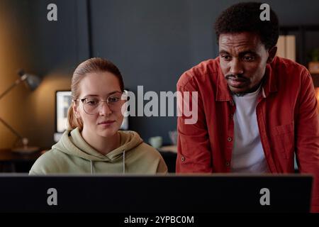 Young female and male colleagues collaborating on project at modern office Two coworkers focused on completing work on laptop while discussing ideas a Stock Photo