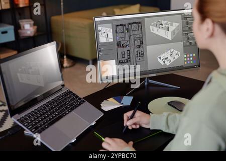 Individual engrossed in creating detailed architectural design on computer using modern digital tools, with another laptop on side for reference and color samples laying on desk Stock Photo