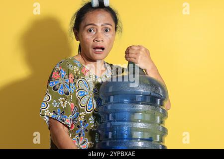 Asian Mom Holding a Five Gallon Bottle of Mineral Water, Isolated on Yellow Background Stock Photo