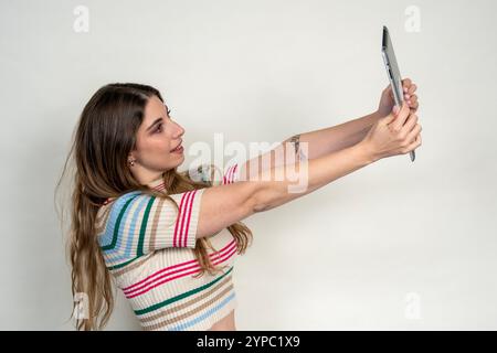 Young woman holding a tablet and taking a selfie with a surprised expression on her face Stock Photo