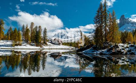 Vibrant autumn hues from the surrounding forest mirror perfectly in the calm waters of Lago Federa, with Rifugio Palmieri nestled against the backdrop Stock Photo