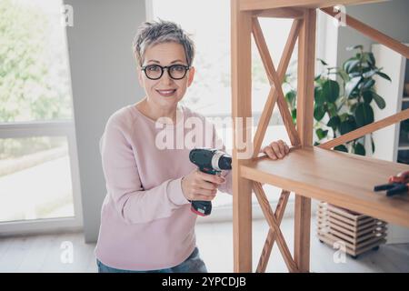 Photo of shiny cute woman dressed pink sweatshirt fixing shelf indoors house apartment room Stock Photo